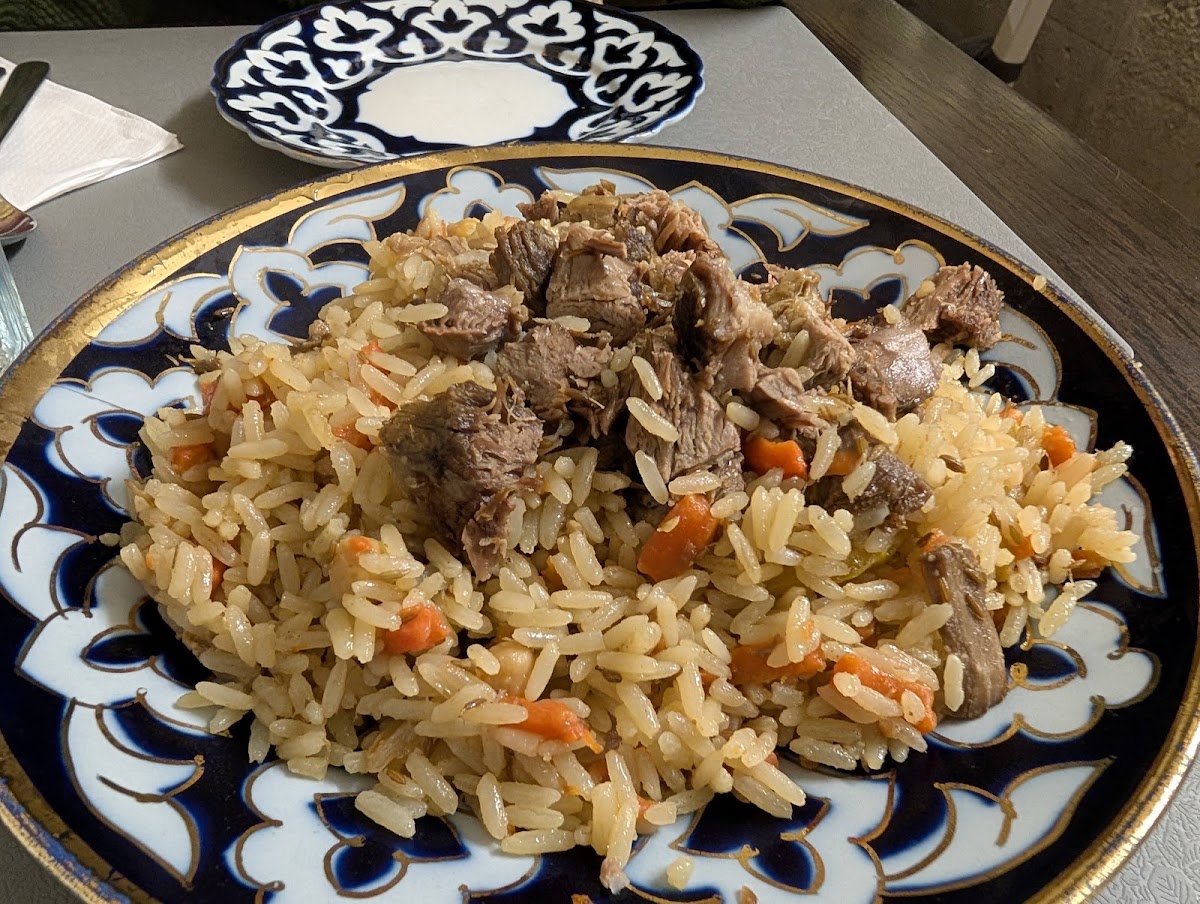 Rice cooked with carrot and cumin, piled with chunks of lamb, served on a large cobalt-blue plate patterned in white and gold.